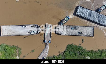 Vue aérienne de haut en bas de remorqueurs et de barges chargeant du sable et du gravier sur une rivière boueuse en Indonésie Banque D'Images