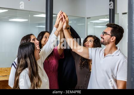 Groupe de six collègues collaborent et célèbrent leurs réalisations dans un espace de coworking moderne. La scène montre divers individus engagés dans l'équipe Banque D'Images