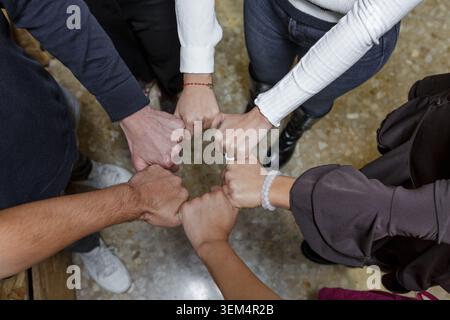 Un groupe d'individus dans un espace de coworking se joignent à poings dans une démonstration d'unité et de collaboration. Ce moment capture l'esprit de travail d'équipe parmi les professés Banque D'Images