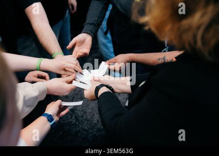 Groupe diversifié de personnes dans un cercle dessinant des notes de papier ou des billets de tombola pour un jeu de consolidation d'équipe Banque D'Images