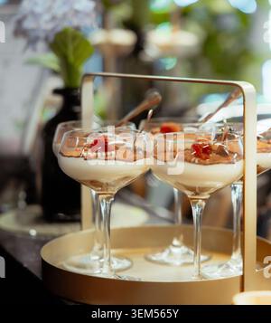 Tiramisu dans des verres coupés avec de la crème de mascarpone, du saupoudrage de cacao et des framboises sur un présentoir en or lors d'un mariage ou d'un événement de restauration de luxe Banque D'Images
