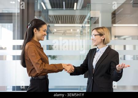 Deux femmes d'affaires souriantes se serrent la main dans un bureau moderne lumineux, célébrant le partenariat, l'accord et le travail d'équipe confiant, des collègues professionnels forgeant une collaboration réussie Banque D'Images
