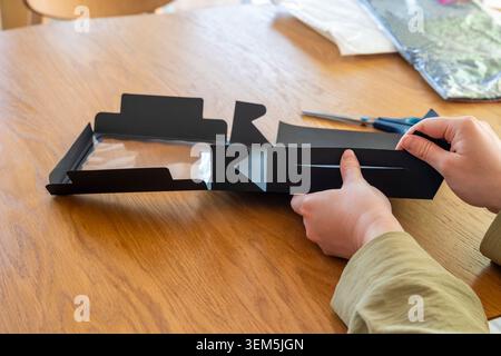 Mains pliant une boîte cadeau en carton noir sur une table en bois à la lumière du jour ensoleillé. Concept : emballage e-commerce Banque D'Images