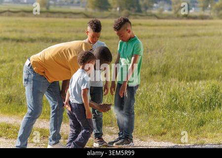 Un père applique un insectifuge à ses enfants à l'extérieur pendant une journée d'été à la campagne pendant qu'ils se préparent à s'amuser en famille. Banque D'Images
