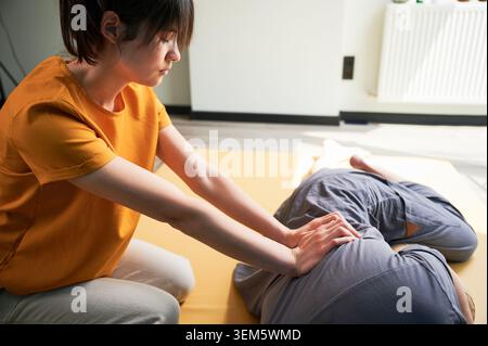 Masseuse faisant massage yoga thaïlandais. Femme thérapeute faisant le traitement de massage traditionnel pour le patient masculin à l'intérieur. Client allongé sur tapis, méditant, profitant d'un massage des mains dans une atmosphère calme. Banque D'Images
