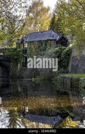 Vue d'une charmante maison en pierre couverte de lierre reflétée dans les eaux calmes d'un canal à côté d'un pont historique à Lancaster, Angleterre, Royaume-Uni. Banque D'Images