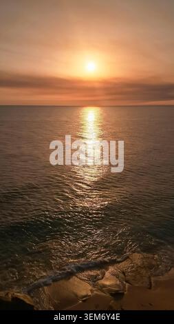 La lumière du soleil Golden Hour illumine un paysage marin serein avec un brillant chemin de soleil reflétant les ondulations, créant une atmosphère paisible et chaleureuse Banque D'Images
