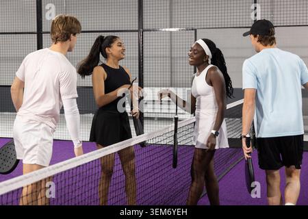 Divers joueurs en jupes et shorts échangeant des salutations au filet sur le court violet tenant des pagaies Banque D'Images