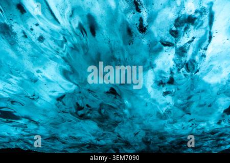 Gros plan abstrait de la texture du plafond des grottes de glace glaciaires en Islande montrant des motifs tourbillonnants de glace bleu-blanc entrecoupés de dépôts de cendres volcaniques sombres Banque D'Images