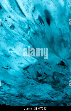 Gros plan vertical de la texture bleue et blanche des grottes de glace glaciaire en Islande avec des inclusions de cendres volcaniques sombres créant des motifs tourbillonnants abstraits à travers le t Banque D'Images