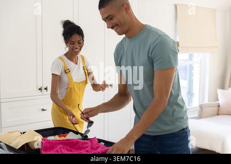 Divers couples emballant une valise dans la chambre, femme portant une salopette jaune, homme tenant des lunettes de soleil Banque D'Images