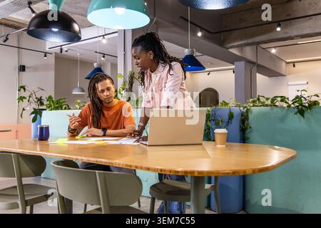 Divers collègues collaborant au centre de coworking, se penchant sur la table commune avec un ordinateur portable, des papiers Banque D'Images