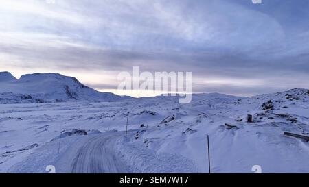 Un paysage montagneux enneigé à couper le souffle en Norvège avec une route sinueuse, un ciel hivernal tranquille et une nature intacte Banque D'Images