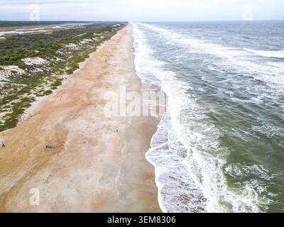 La plage présente un sable doux et doré qui rencontre des eaux turquoises claires. Des vagues douces se jettent sur le rivage, créant une atmosphère tranquille parfaite pour rela Banque D'Images