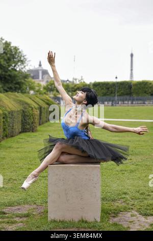Jeune ballerine en tutu noir et léotard bleu effectue une pose gracieuse tout en étant assise sur un piédestal en pierre dans le jardin de Paris avec la Tour Eiffel en arrière-groupe Banque D'Images