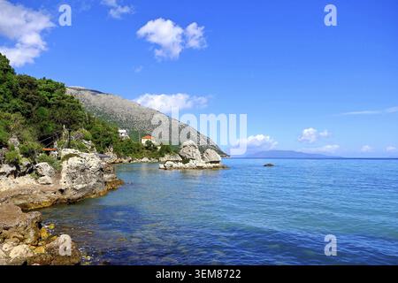 Les eaux turquoises rencontrent un littoral rocheux, une végétation luxuriante et de grands rochers bordent le rivage, avec une montagne offrant une toile de fond spectaculaire Banque D'Images