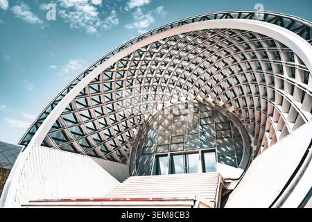 Vue en angle bas d'une structure architecturale futuriste avec une charpente en acier courbée, une façade en verre et des motifs géométriques. Landmar urbain moderne Banque D'Images