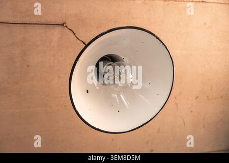 Vue rapprochée d'une suspension vintage en émail avec ampoule LED exposée suspendue au plafond. Luminaire industriel au design rétro, m Banque D'Images