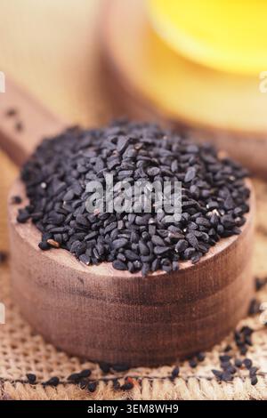 Graines de cumin noir dans une pelle en bois avec de l'huile en arrière-plan Banque D'Images