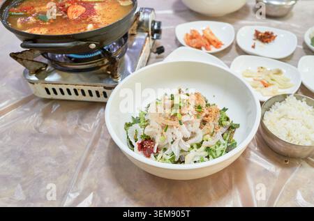 Flet cru tranché avec légumes et pâte rouge, servi avec un ragoût de fruits de mer épicé bouillant et des accompagnements sur une table. Banque D'Images