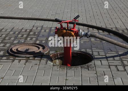 Le couvercle métallique se trouve à côté de l'ouverture. La vanne rouge se connecte au flexible. L'eau coule lentement du bec verseur. Infrastructure urbaine, prête pour l'urgence Banque D'Images