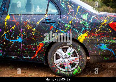 Une berline sombre recouverte de peinture brillante éclaboussure à l'extérieur, avec des éclaboussures sur les portes et les roues, des couleurs vives sur un sol rustique sous la lumière du jour Banque D'Images