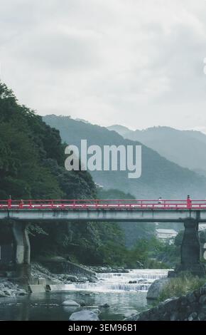 Vue panoramique d'un pont avec des garde-corps rouges sur une rivière de montagne en cascade à Odawara, Japon. Banque D'Images
