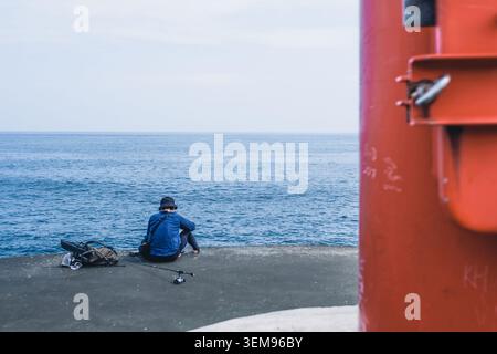 Vue arrière d'un pêcheur pêchant sur un brise-lames en béton à Odawara, Japon. Banque D'Images