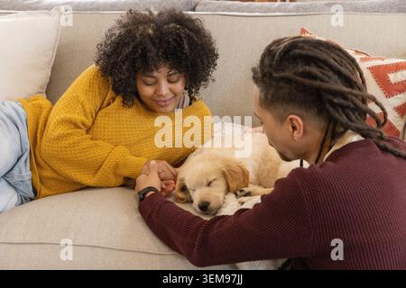 Couple s'inclinant sur le canapé dans le salon, se tenant les mains et caressant dormant chiot Golden retriever Banque D'Images