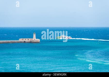 Valletta, Malte – 16 mai 2025 : le catamaran Gozo Fast Ferry « Your Wisdom » navigue près de l’entrée du port historique et du phare, traversant Bright Banque D'Images