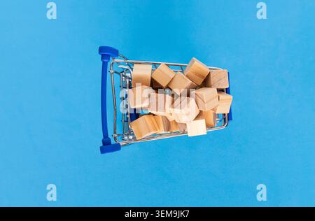 Chariot miniature rempli de blocs de bois sur fond bleu, représentant la logistique de détail Banque D'Images