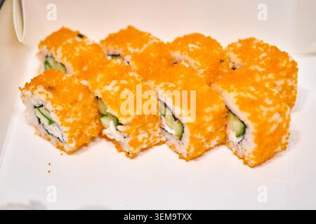 Huit morceaux de rouleaux de sushi makizushi enduits d'œufs de poisson orange vif remplis de concombre et de fromage à la crème sont disposés soigneusement sur la surface blanche un Banque D'Images