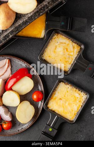 Délicieux fromage à raclette suisse fondu traditionnel sur des légumes cuits ou cuits en dés servis dans des poêles individuelles. Vue de dessus Banque D'Images