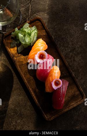 Une vue verticale descendante d'une variété de sushis nigiri de saumon et thon magnifiquement disposés avec des garnitures de radis et du concombre tranché sur un rusti Banque D'Images