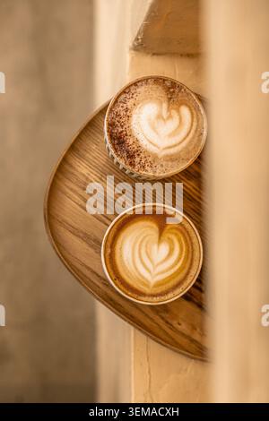 Une photo de haut en bas d'un plateau de service en bois contenant deux boissons chaudes à base d'expresso avec un motif en mousse de coeur distinct, l'une finie avec un saupoudrage de coco Banque D'Images