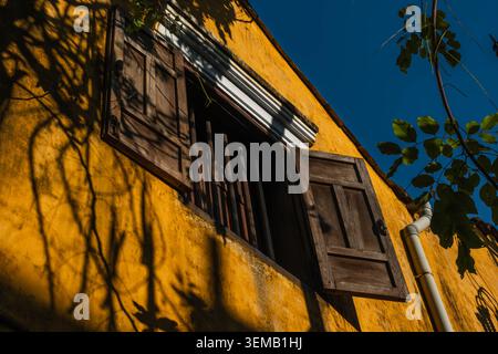 Vieux volets en bois sur un mur jaune vif d'une ancienne maison Banque D'Images