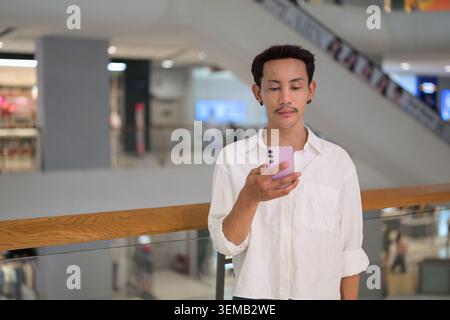 Photographie de paysage et de style de vie professionnelle à la taille de la taille d'un gay thaïlandais non binaire et fluide de genre de la région d'Isan, centrée sur un smartphone rose. Il s Banque D'Images