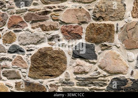 Gros plan de maçonnerie en pierre irrégulière sur le mur extérieur de l'église historique, montrant des textures, des couleurs, des formes et des motifs de mortier variés. Banque D'Images