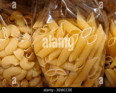 Vue rapprochée de diverses variétés de pâtes sèches stockées dans des sacs en plastique transparents, avec des formes de penne et de coquille aux tons beiges chauds et à la surface texturée Banque D'Images