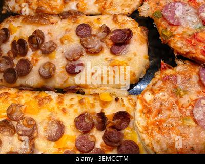 La vue macro montre plusieurs tranches de pizza cuites regroupées sur un plateau sombre. Le fromage fondu recouvre la pâte, les ronds de pepperoni bruns parsèment la surface et Smal Banque D'Images