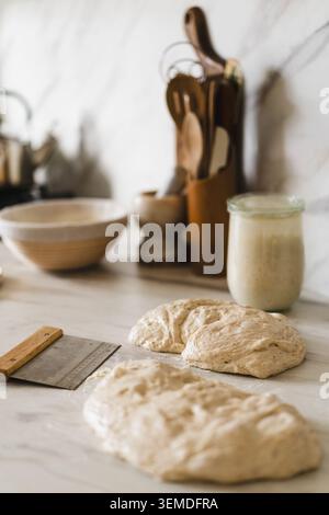 Levain la pâte à pain au levain repose sur un comptoir de cuisine en marbre, prêt à être pétri. Un pot de levain au levain actif se trouve à proximité, entouré par Banque D'Images