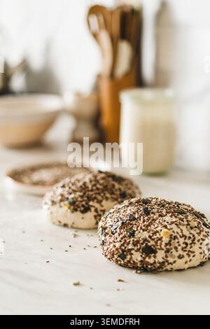 Pâte à pain au levain saupoudrée de graines sur un comptoir de cuisine, prête pour la cuisson. Une approche rustique et maison de la fabrication artisanale classique du pain. Banque D'Images