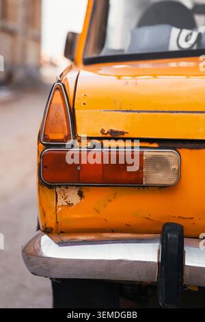 Gros plan d'un feu arrière et d'un pare-chocs jaunes de voiture de l'ère soviétique, montrant de la rouille et de la peinture usée. Détails urbains nostalgiques évoquant l'histoire du CCCP et le froid Banque D'Images