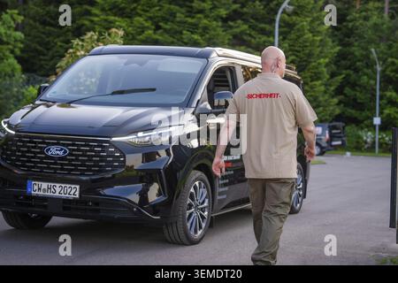 Un homme en uniforme de sécurité marche à côté d'une camionnette noire devant un espace vert, Revier Dienst BEI Bjoern Hartmann Sicherheit, Calw District, Allemagne Banque D'Images