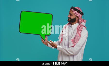 Jeune adulte tenant la bulle de discours sur la caméra, créant la publicité Web pour le nouveau marketing promotionnel. Gars arabe travaillant sur le slogan commercial avec icône en carton vierge, panneau d'affichage signe. Banque D'Images