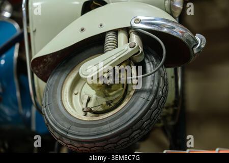 La vue détaillée en bas angle capture la roue avant, le système de suspension et l'aile du scooter vintage. La carrosserie vert clair est décorée de garnitures contrastantes chromées polies Banque D'Images
