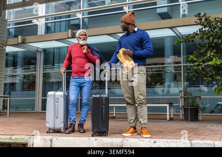 Debout deux hommes avec des valises portant des chandails rouges et bleus sur la plaza, avec sac en papier, écouteurs Banque D'Images