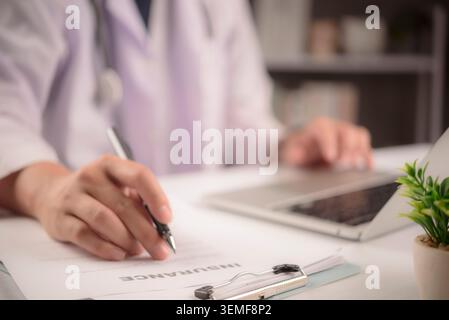 Médecin signant le formulaire de contrat d'assurance maladie sur le presse-papiers. Concept de soins médicaux montrant le médecin remplissant le document de police, les documents de réclamation, Banque D'Images