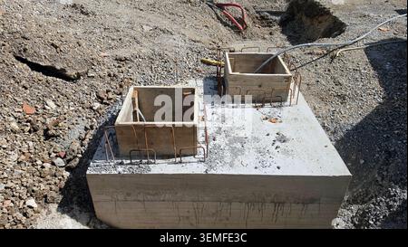 Une paire de coffrages temporaires en bois reposent sur une base de béton solide fraîche avec des boucles de renforcement en métal courbées sur un chantier de construction en terre battue Banque D'Images