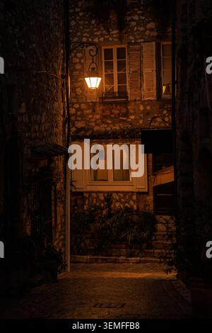 Une vue imprenable en soirée donnant sur une étroite rue pavée entre de vieux bâtiments en pierre, illuminée par une lanterne murale classique. Banque D'Images